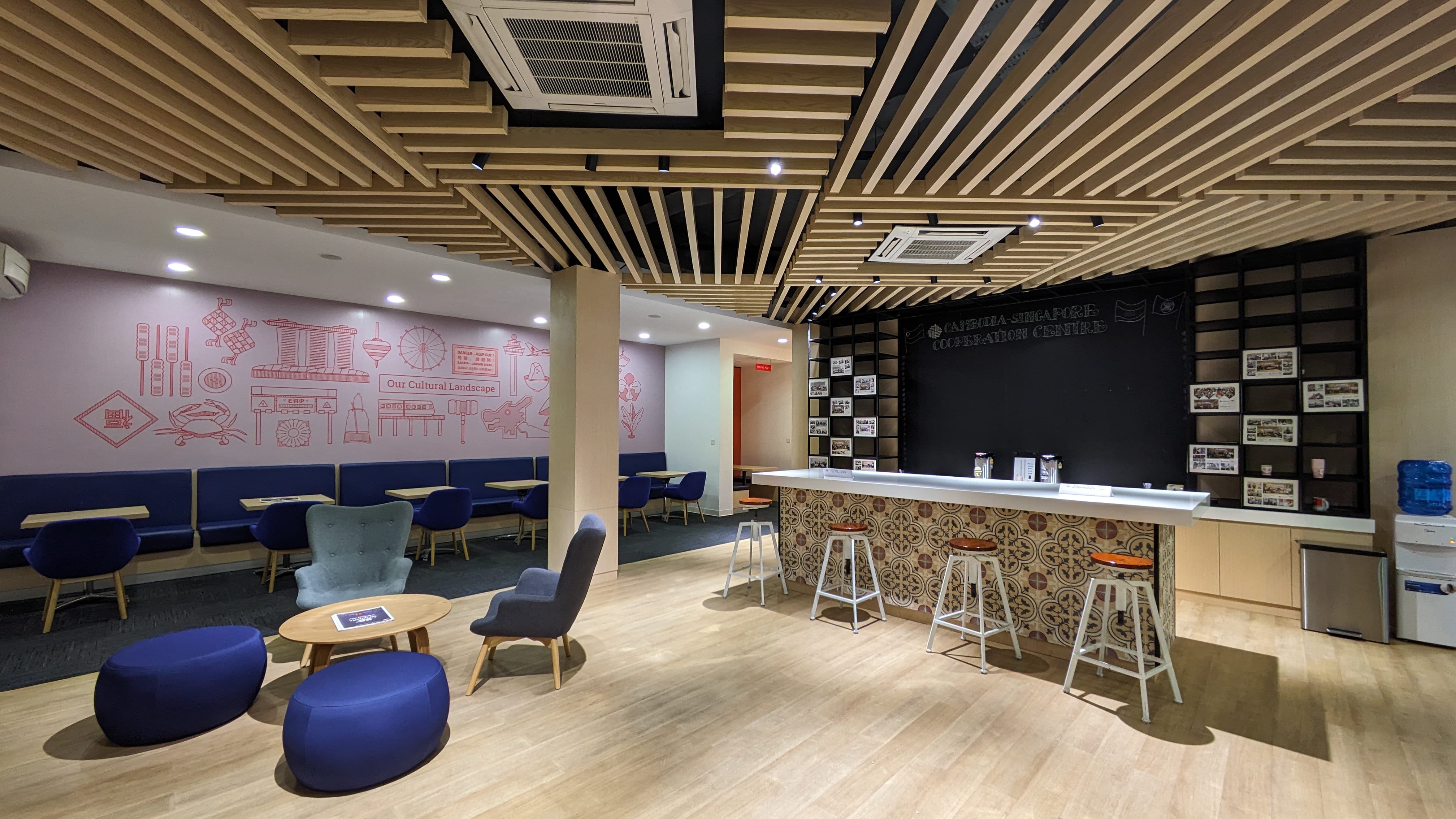 Office lounge area with bar, seating, and light wood ceiling detail; wall art depicting Singapore.